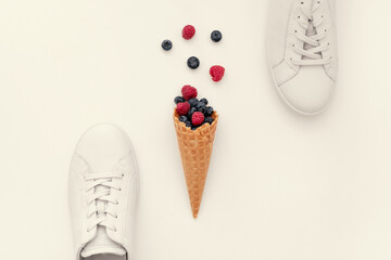 White women's sneakers and a horn with summer berries on a light background, close-up, minimal, art, modern. The concept is the enjoyment of quality shoes. Flat lay, top view