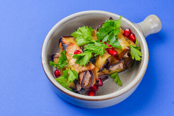 Egg-plant rolls with meat and pomegranate seeds served in a bowl over blue background.