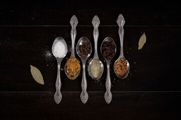 different spices and spices on a spoon on a dark wood background
