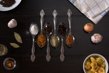 different spices and spices on a spoon on a dark wood background