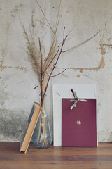 still life in the form of a glass transparent vase with dried grass and books on the background of a vintage wall