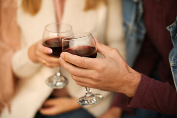 Two glasses of red wine close-up in hands outside the house. Man and woman in love make the clink of glasses. Celebrate Valentine's Day, date. Warm, blurred background, countryside relaxation.