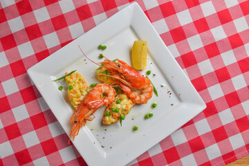 Fresh organic shrimp cocktail with mayonnaise salad. Served on a white plate over red plaid tablecloth.