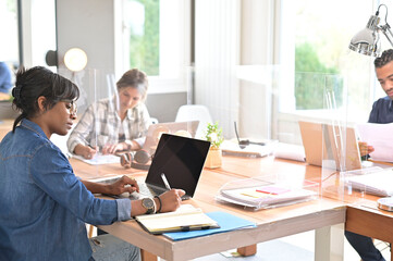 View of co-workers in open space office protected by plexiglas