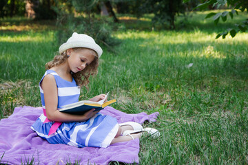 little happy girl in a dress in the park on the grass reads a book