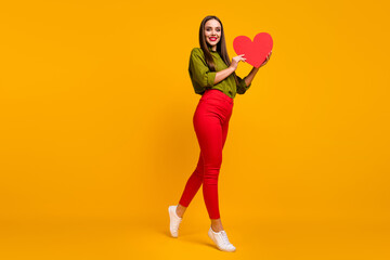 Fototapeta na wymiar Full length body size view of lovely slim cheerful girl holding in hands heart walking isolated on bright yellow color background