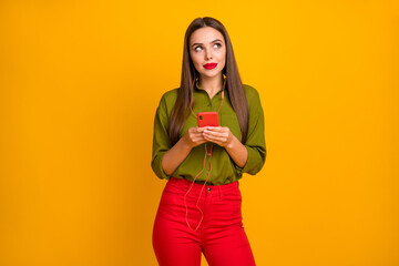 Portrait of glamorous minded dreamy straight-haired girl using gadget listening podcast isolated over bright yellow color background