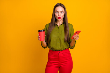 Portrait of pretty coquettish straight-haired girl drinking latte sending air kiss using cell 5g isolated over bright yellow color background