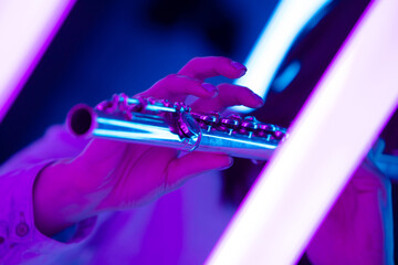 Flute in female hands. Fingers touch flute keys close up. Wind instrument against the background of bright neon lights. Poster for advertising a music school. © kinomaster