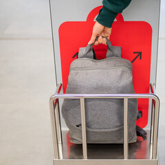 Woman checking backpack metal cage checking carry-on luggage at airport.