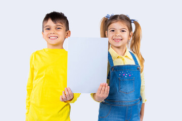 Cute children with a happy smile are posing with a white sheet of paper for your advertisement.