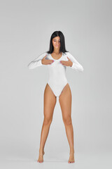 beautiful slim tanned woman with perfect body and long legs in white bodysuit posing over studio...