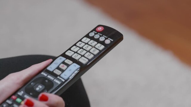 Une femme avec du vernis &agrave; ongle rouge utilise une t&eacute;l&eacute;commande.