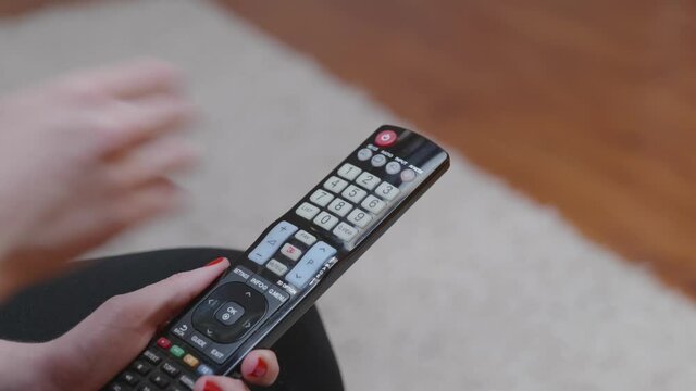 Une femme avec du vernis &agrave; ongle rouge utilise une t&eacute;l&eacute;commande.