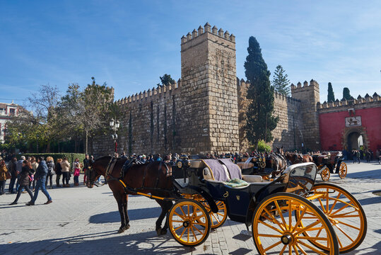 Seville, Andalusia, Spain, Europe. Horse carriage and view of the Lion's Gate in the Real Alcazar of Seville and row of people waiting to enter