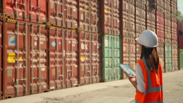 Asian engineer Foreman female worker working checking at Container cargo harbor holding tablet device to loading cargo containers. Dock female worker  Logistics import export shipping yard concept.
