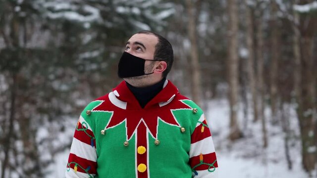portrait of a young man in a Christmas sweater, wearing a mask, looks around, in the middle of the forest.