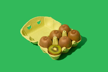 Kiwi fruit in an egg carton on green background. Creative food concept.