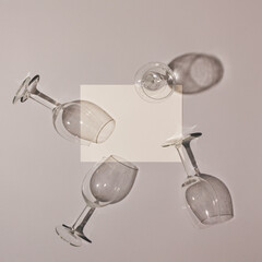 Empty wine glasses with shadows and white paper card note on a grey background. Minimal aesthetic idea.