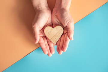 Hands holding wood heart on blue and orange color paper background, health care, love, organ donation.