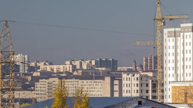 Crane and building construction site in a big city aerial timelapse during all day. Workers laying briks walls of new residential appartment house near high voltage power lines tower