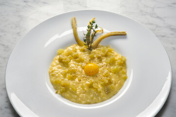 risotto with thistles and egg in white plate on marble top in top view