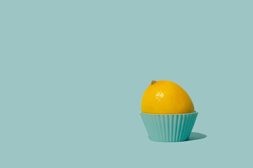 Sunlit lemon in a cyan cupcake cup on a cyan background. Minimal summer idea.