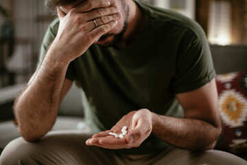 Sad unhappy depressed man is holding a pill in a hand. Desperate young man holding handful of pills..