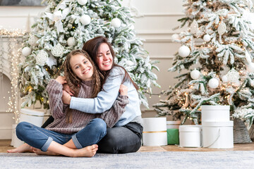 Two sisters sit under the tree and happily hug each other, a good family tradition for the new year