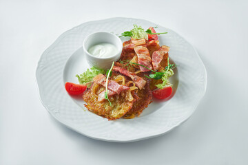 Appetizing potato pancakes (deruny) with bacon and sour cream in a white plate on a white plate. Ukrainian food