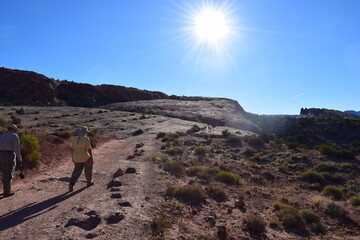 Man hiker with hat hiking on desert path towards into sun