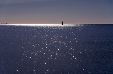Beautiful peaceful seascape with small ship and lighthouse silhouette on the sea horizon