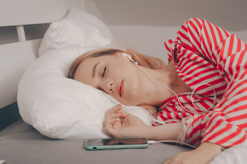 The girl lies on the bed with closed eyes asleep. Woman with headphones and phone, listening to...