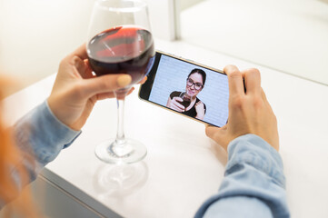 The women talk over video communication on the phone and drink red wine. The quarantined girl is not making a video call