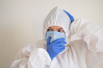 Frightened woman in a protective suit, mask and gloves holds her head. Fear in the eyes of a virologist doctor