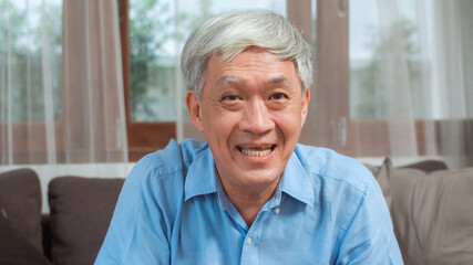 Fototapeta na wymiar Asian senior man video call at home. Asian senior older Chinese male using mobile phone video call talking with family grandchild kids while lying on sofa in living room at home concept.