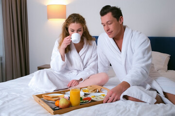 Family on vacations resting in their room. Young couple in bathrobes having a breakfast together...