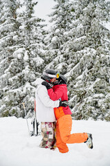 Fototapeta na wymiar Young couple of tourists kissing in snow against mesmerizing snowy spruce forest on background. Vivid colorful suits on white snow. Concept of skiing and relationships.