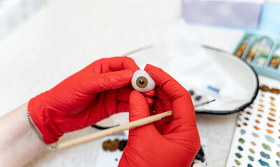 Artificial plastic human eye in doctor's hands. Eyes transplantation. Eye prosthesis. Closeup.