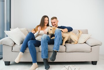 Young happy couple with dog sitting on sofa