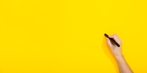 Black marker in female hand writes on a blank yellow background with copy space, text place....