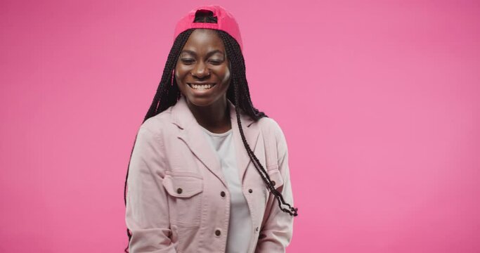 Portrait of joyful young African American pretty female wearing red cap stands isolated over pink background in positive mood posing to camera making funny moves and face expression. Model concept