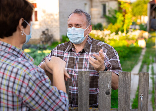 Farm Neighbors In Protective Masks Talk At The Border Of Garden Plot