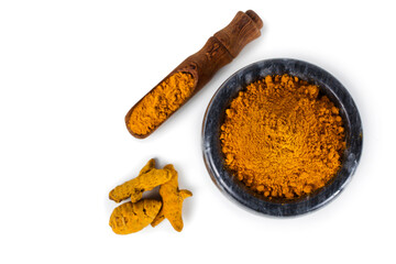 Turmeric powder spice heap in a black stone bowl with turmeric roots and bamboo scoop isolated on a white background. Top view.