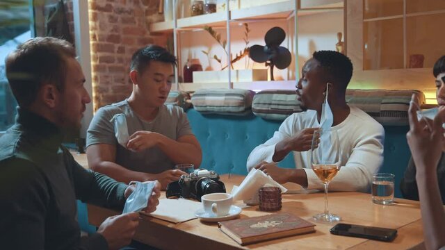 New normal. Happy diverse people taking off their protective masks while coming at the cafeteria. Multiracial friends preparing to drinking beverages and eating dishes at the cafe. Friendship concept