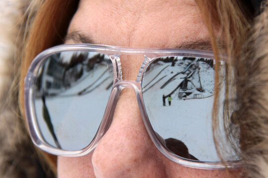 Verspiegelte Sonnenbrille einer Frau spiegelt Skigebiet wieder