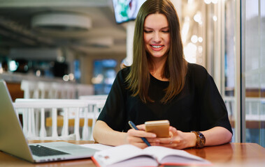 Smiling adult freelancer messaging via smartphone in contemporary cafeteria