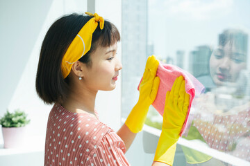 Maid service woman wearing yellow protection gloves cleaning glass window with dry rag.