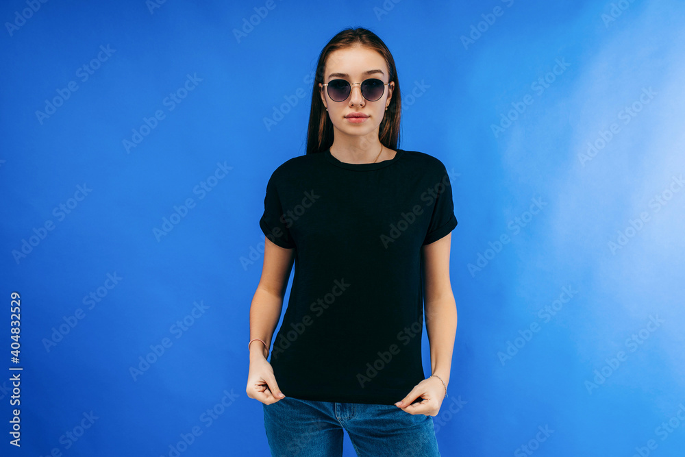 Canvas Prints stylish girl in glasses wearing black t-shirt posing in studio on blue background