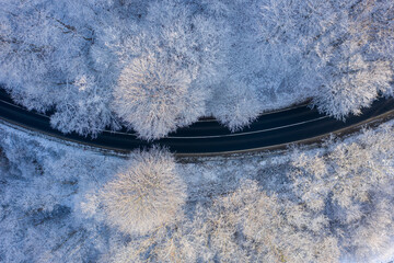 Csesznek, Hungary - Aerial top down view of winter forest crossed by asphalt road. Snowy landscape background.